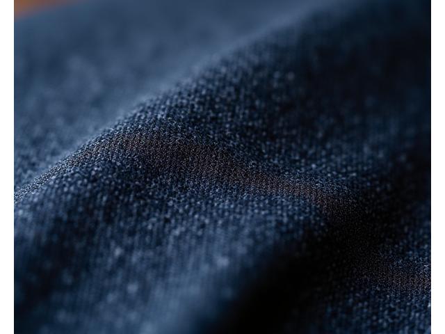 Detail tekstur kain jas pria premium dengan pencahayaan lembut.