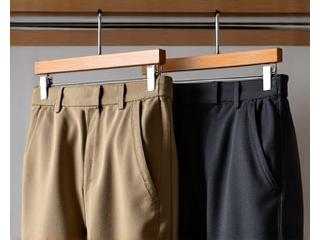 Tampilan dekat lipatan rapi celana chino warna khaki dan celana bahan wol abu-abu pada gantungan di lemari pakaian pria.